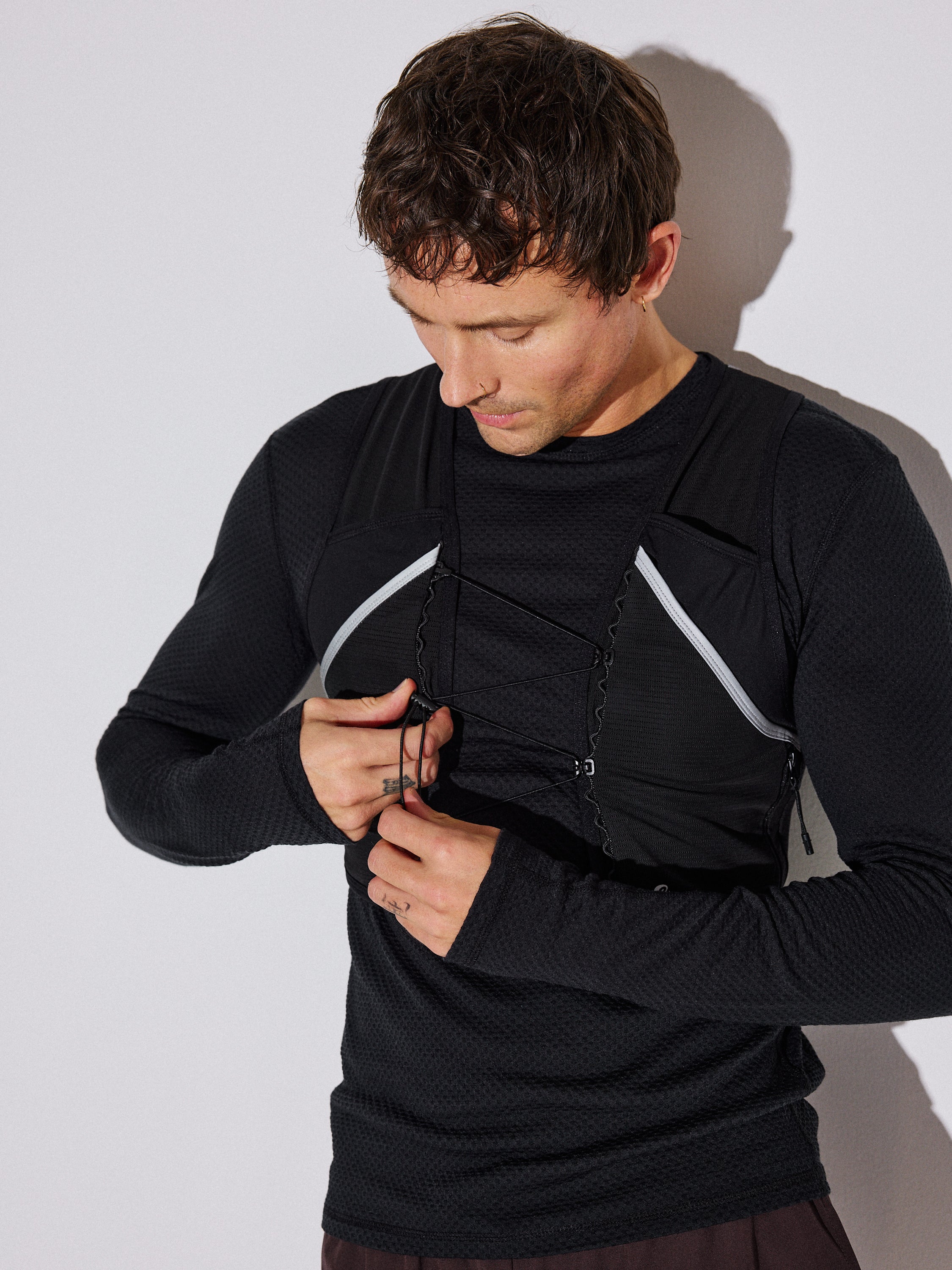A man wearing a black long-sleeve athletic compression shirt with white curved trim and front zipper details, shown against a plain light gray background.