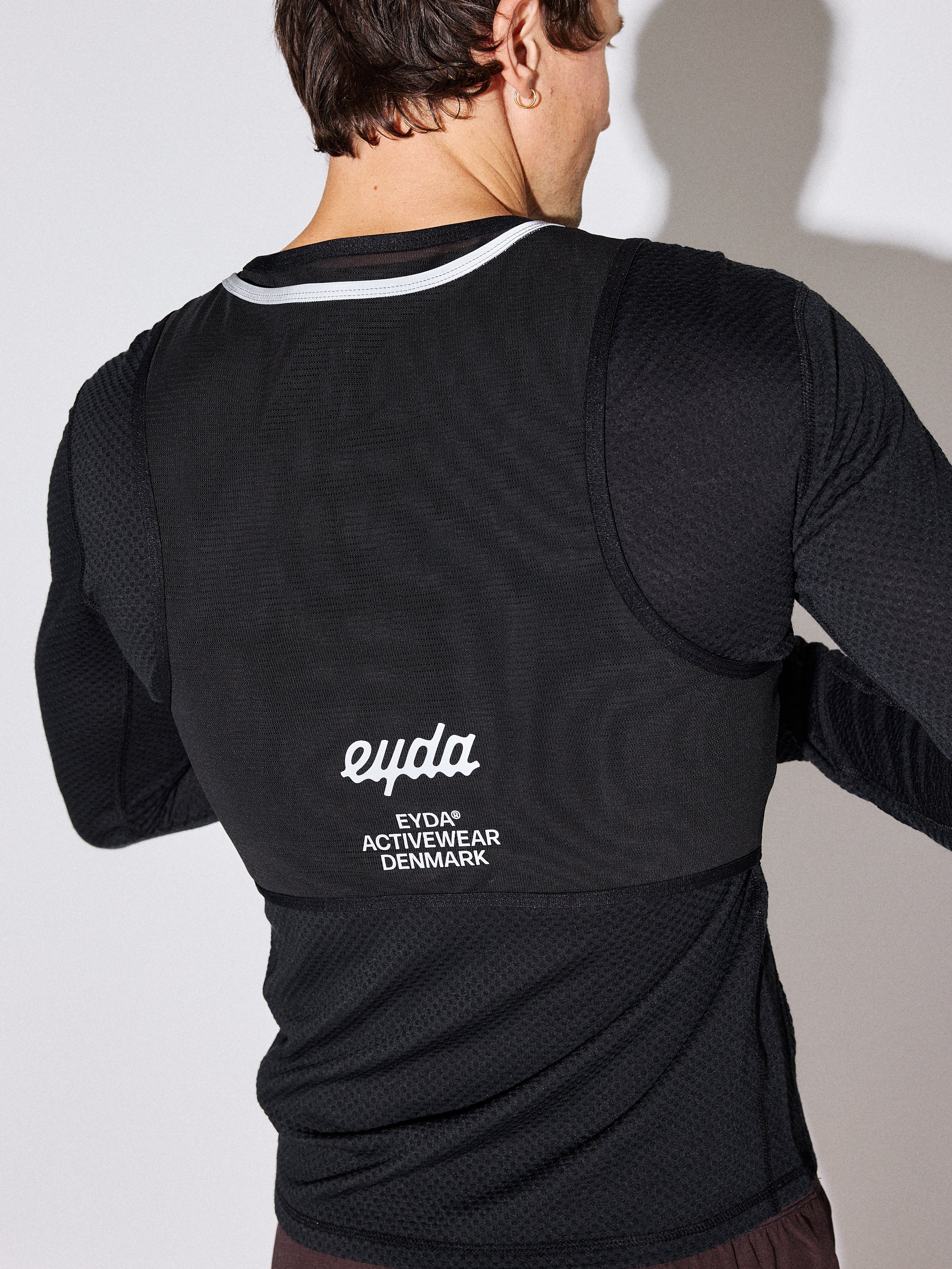 A man wearing a black long-sleeve athletic shirt, shown from the back. The shirt features a white logo and text reading 'eyda' and 'EVDA ACTIVWEAR DENMARK' on the back.